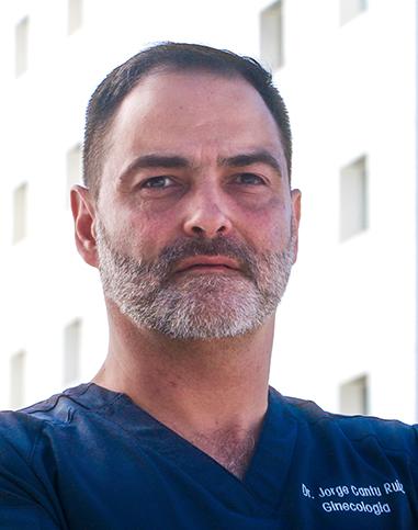 Es la foto de perfil de un ginecólogo y obstetra en Torreón de Hospital Angeles Torreón. Usa un uniforme médico color azul. Tiene el cabello negro y la barba blanca.