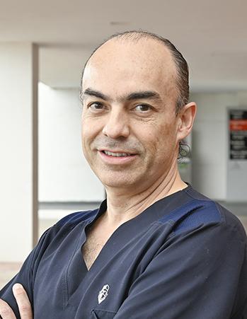 Es la foto de perfil de un cirujano plástico en León de Hospital Angeles León. Utiliza un uniforme azul marino, tiene los brazos cruzados y está sonriendo.
