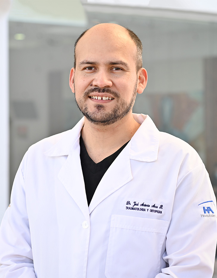 Es la foto de perfil de un ortopedista, traumatólogo y artroscopista en Tijuana de Hospital Angeles Tijuana. Usa una bata blanca y un uniforme médico negro. Su barba es de color gris oscuro. Está sonriendo.