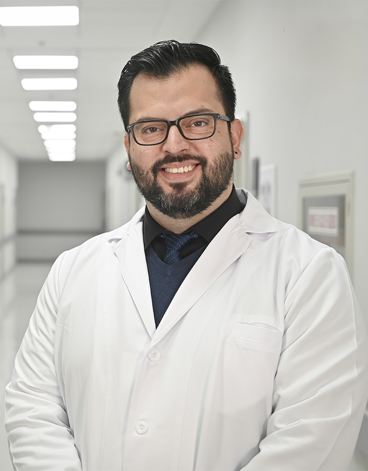 Es la foto de perfil de un anestesiólogo en Ciudad de México de Hospital Angeles Universidad. Usa una bata blanca con una camisa negra. Tiene el cabello y la barba negra. Está sonriendo.