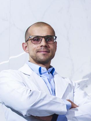 Es la foto de perfil de un ginecólogo y obstetra en Ciudad de México de Hospital Angeles Universidad. Usa una bata blanca y camisa azul. Tiene los brazos cruzados y una ligera sonrisa.