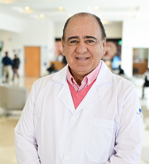 Es la foto de perfil de un urólogo en Xalapa de Hospital Angeles. Usa una bata blanca y una camisa gris. Tiene parte de su cabello negro. Tiene los brazos cruzados.