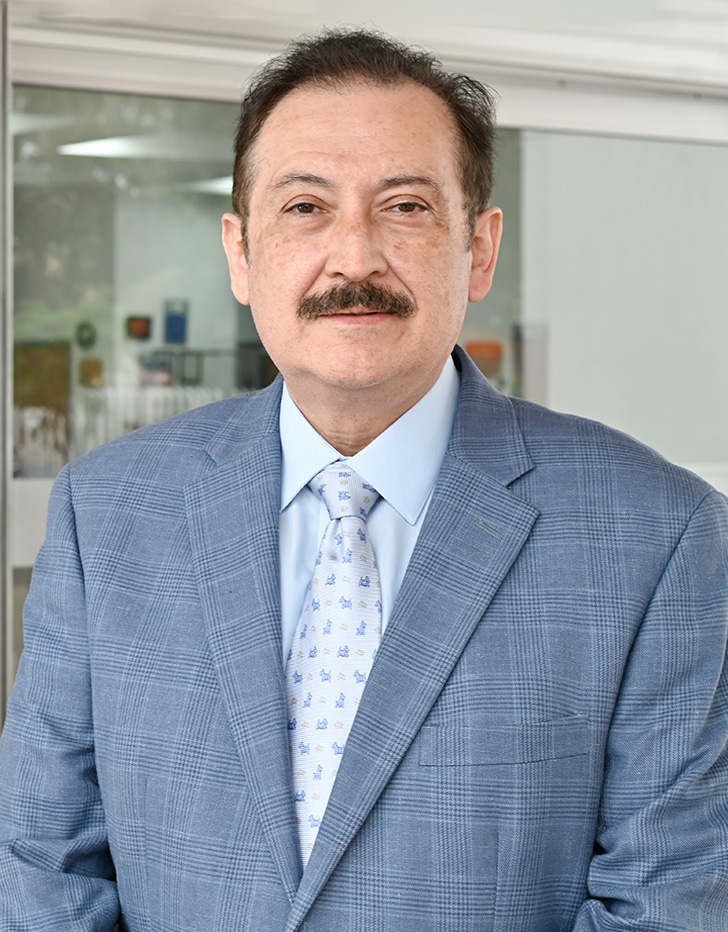 Es la foto de perfil de un ortopedista y traumatólogo en Tijuana de Hospital Angeles. Usa una chamarra azul marino y una camisa azul claro. Tiene el cabello y bigote negro.