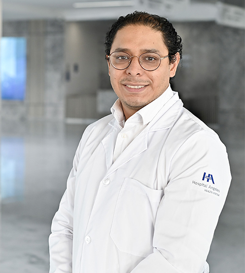 Es la foto de perfil de un neumólogo en Querétaro de Hospital Angeles Centro Sur. Viste un traje beige con una camisa negra y lunares negros. Usa lentes y está sonriendo.