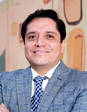 Es la foto de perfil de un urólogo en Ciudad de México de Hospital Angeles Lindavista. Tiene el cabello negro. Usa un saco color gris con líneas azules y una corbata azul de cuadros.