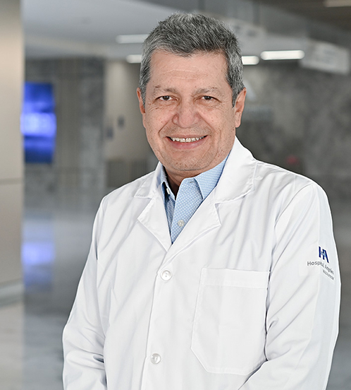 Es la foto de perfil de un cirujano oncológico en Querétaro de Hospital Angeles Centro Sur. Usa una bata blanca, una camisa amarilla pastel y tiene el cabello canoso.