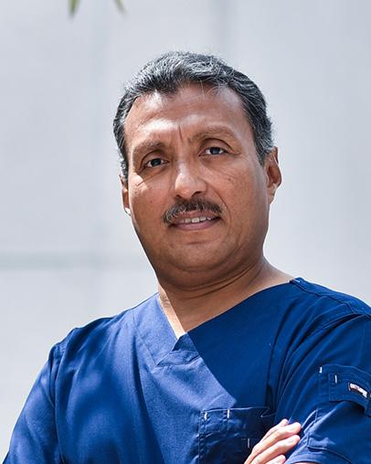 Es la foto de perfil de un pediatra y cirujano pediátrico en Villahermosa de Hospital Angeles. Usa un uniforme médico azul. Tiene el cabello y bigote negro. Tiene los brazos cruzados.