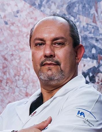 Es la foto de perfil de un cirujano oncólogo y cirujano general en San Pedro Garza de Hospital Angeles Valle Oriente. Usa una bata blanca con uniforme médico negro. Tiene los brazos cruzados.