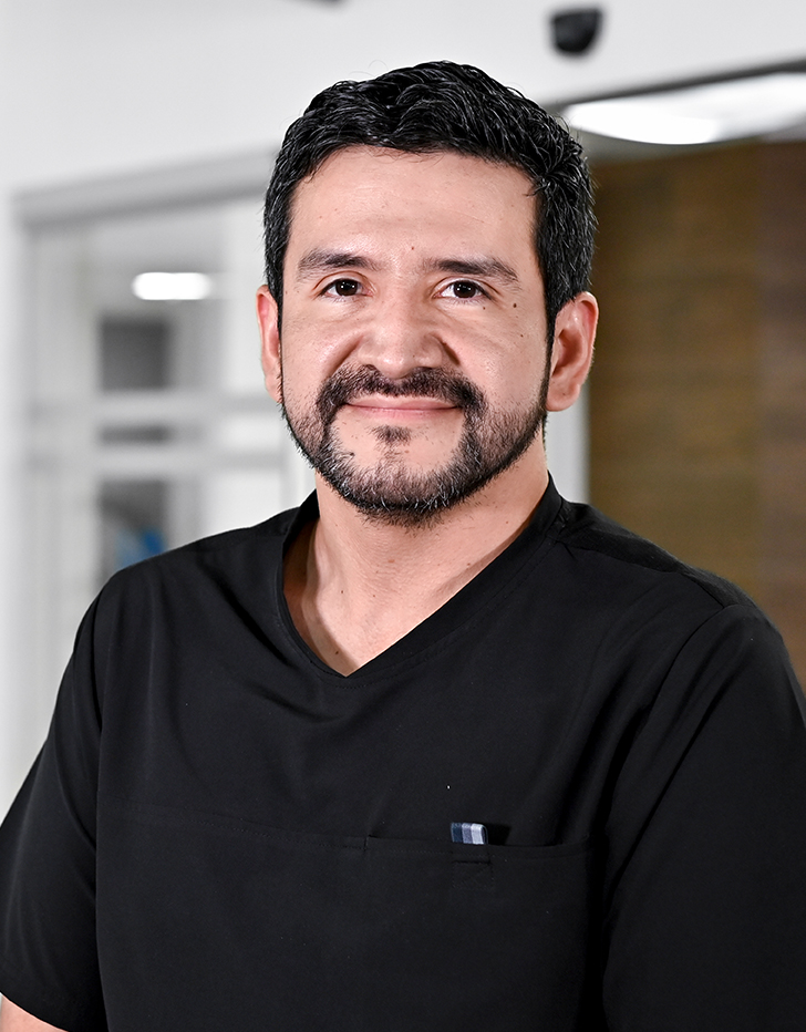 Es la foto de perfil de un urólogo en Ciudad de México de Hospital Angeles Santa Mónica. Usa un uniforme médico negro. Tiene el cabello y barba negro. Está sonriendo.