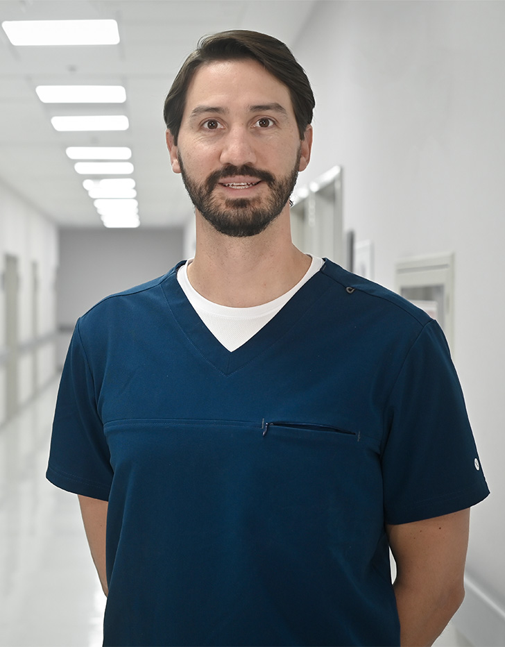 Es la foto de perfil de un ginecólogo y obstetra en Ciudad de México de Hospital Angeles Universidad. Usa un uniforme médico azul con una playera blanca. Tiene el cabello y barba negra.