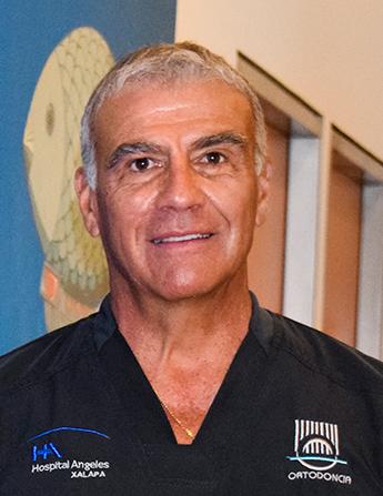 Es la foto de perfil de un ortodoncista en Xalapa de Hospital Angeles. Usa un uniforme médico negro. Tiene el cabello gris. Está sonriendo.