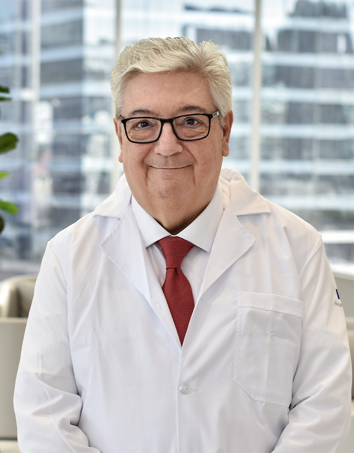 Es la foto de perfil de un oncólogo médico en San Pedro Garza de Hospital Angeles Valle Oriente. Usa una bata blanca, camisa blanca y corbata roja. Tiene el cabello gris y usa lentes.