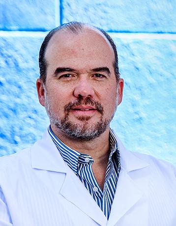 Es la foto de perfil de un cirujano general en León de Hospital Angeles León. Utiliza una bata blanca, camisa blanca, tiene barba de candado canosa.