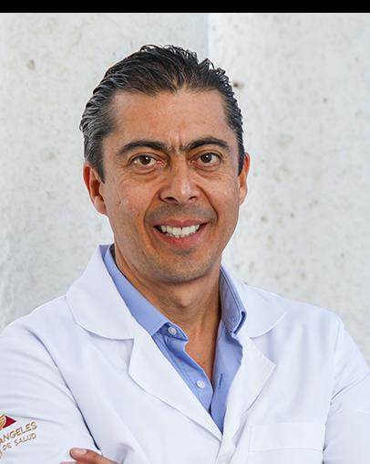 Es la foto de perfil de un neurólogo pediátrico en León de Hospital Angeles León. Usa una bata blanca con una camisa azul, tiene los brazos cruzados y está sonriendo.