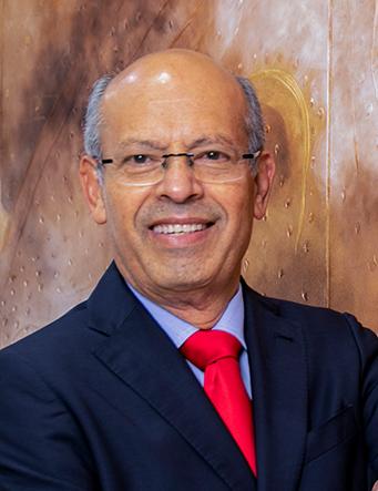 Es la foto de perfil de un cirujano general en León de Hospital Angeles León. Usa un saco negro, camisa azul cielo y corbata roja. Tiene lentes y está sonriendo.