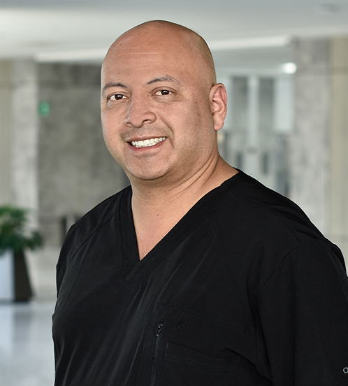 Es la foto de perfil de un cirujano general y angiólogo especialista en cirugía vascular y endovascular en Querétaro de Hospital Angeles Centro Sur. Usa un uniforme negro, es calvo y está sonriendo. 