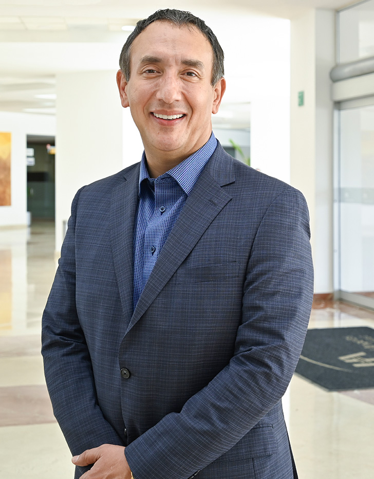 Es la foto de perfil de un cirujano neurológico en Ciudad Juárez de Hospital Angeles Ciudad Juárez. Trae puesto un traje azul marino con camisa y está sonriendo.