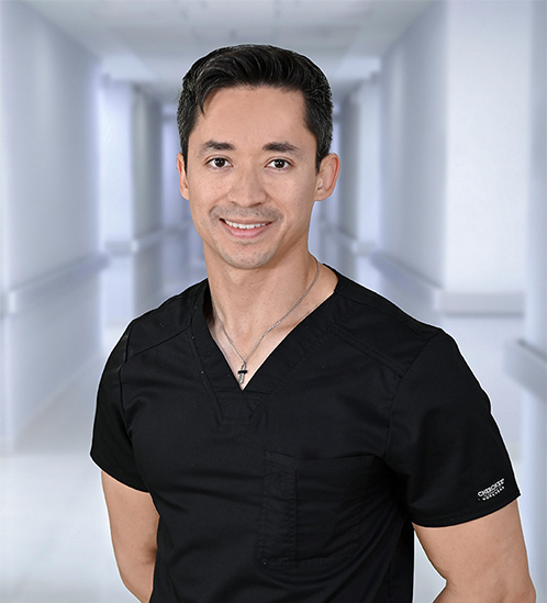 Joven médico sonríe vistiendo pijama quirúrgica negra, de pie frente a un pasillo de Hospital Angeles, la mejor red de hospitales privados de México.