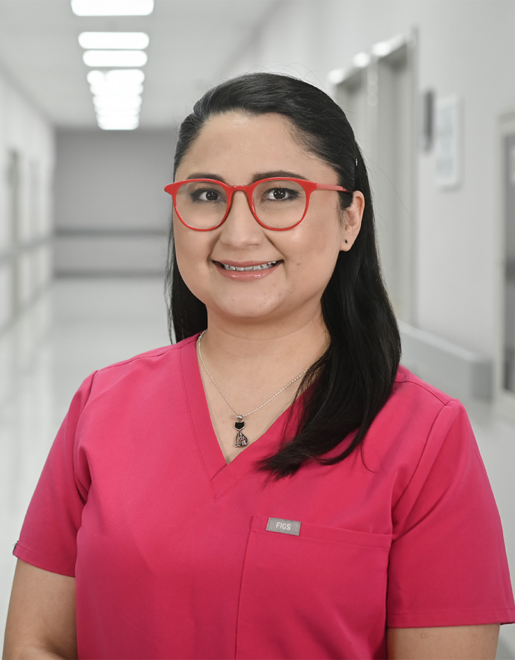 Es la foto de perfil de una pediatra, alergóloga pediátrica y alergóloga en Ciudad de México de Hospital Angeles Universidad. Usa un uniforme meédico rosa. Tiene el cabello negro y usa lentes rojos. Está sonriendo.