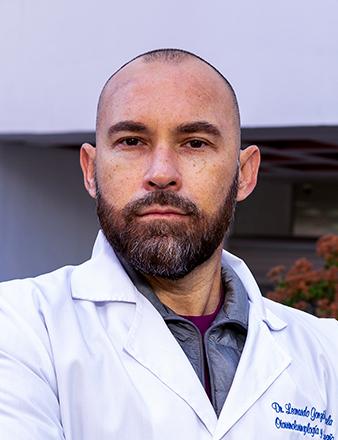 Es la foto de perfil de un otorrinolaringólogo en Tijuana de Hospital Angeles. Usa una bata blanca con una camisa azul. Tiene barba café oscuro. Está serio.