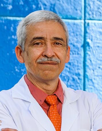 Es la foto de perfil de un reumatólogo en León de Hospital Angeles León. Utiliza una bata blanca, una camisa roja y una corbata naranja. El doctor tiene el cabello canoso y usa bigote.