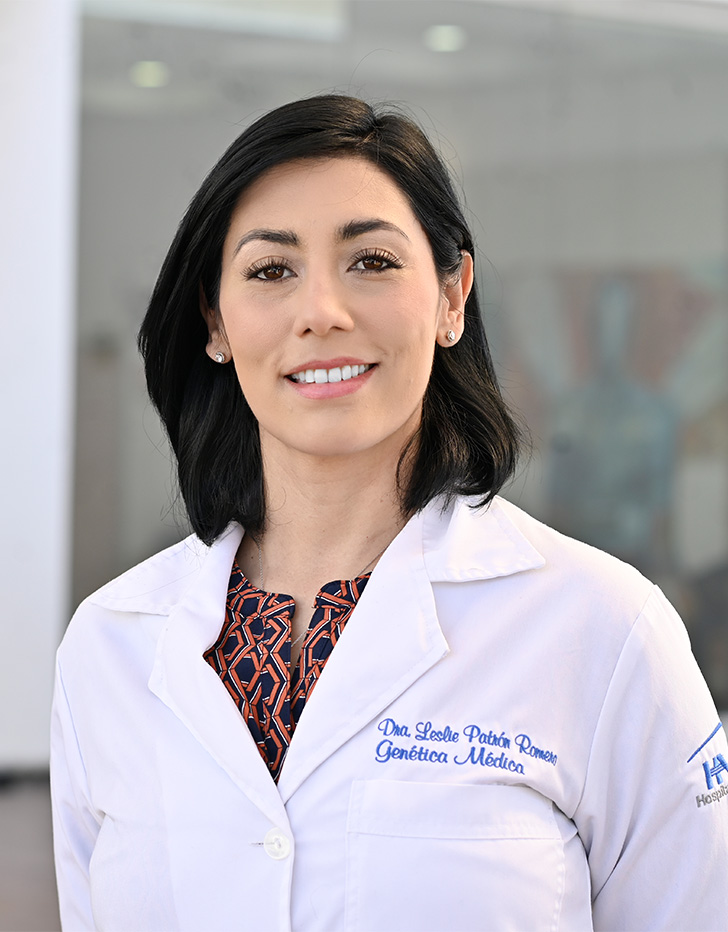 Es la foto de perfil de una genetista en Tijuana de Hospital Angeles. Usa una bata blanca con una blusa café. Tiene el cabello corto y negro. Está sonriendo y tiene los brazos cruzados por detrás.