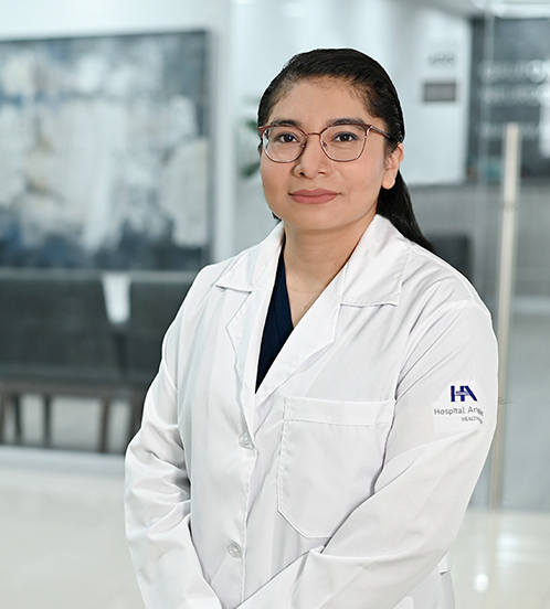 Es la foto de perfil de una internista en Ciudad de México de Hospital Angeles Acoxpa. Usa una bata blanca con un uniforme médico azul oscuro. Tiene el cabello chino y recogido.