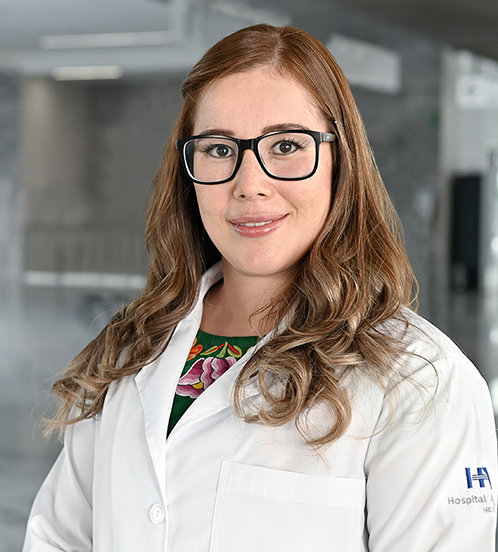 Es la foto de perfil de una ortopedista y traumatóloga en Querétaro de Hospital Angeles Centro-sur. Usa lentes, una blusa verde con flores y una bata blanca. Tiene el cabello castaño y ondulado.