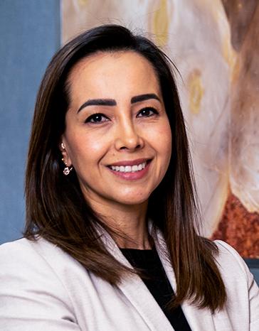 Es la foto de perfil de una ginecóloga y obstetra en León de Hospital Angeles León. Utiliza una bata blanca con una blusa negra. Su cabello es lacio y la doctora está sonriendo.