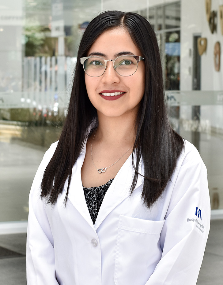 Es la foto de perfil de una médica en medicina de rehabilitación en Ciudad de México de Hospital Angeles Acoxpa. Usa una bata blanca con una blusa negra. Usa accesorios plata, lentes y un labial color ladrillo.