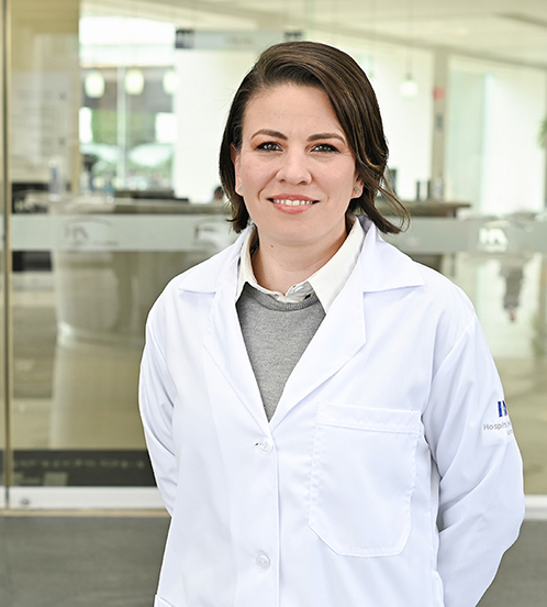 Es la foto de perfil de una psiquiatra en Ciudad de México de Hospital Angeles Acoxpa. Usa una bata blanca con un sueter gris y una blusa blanca. Tiene el cabello corto y café.