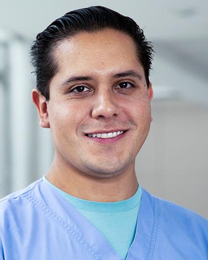 Es la foto de perfil de un angiólogo y cirujano vascular y endovascular en Huixquilucan de Hospital Angeles Lomas. Usa un uniforme azul con una playera verde. está sonriendo amablemente.