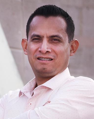 Es la foto de perfil de un neurólogo pediátrico en Torreón de Hospital Angeles. Usa una camisa rosa pastel. Tiene el cabello negro y está sonriendo. Tiene los brazos cruzados.