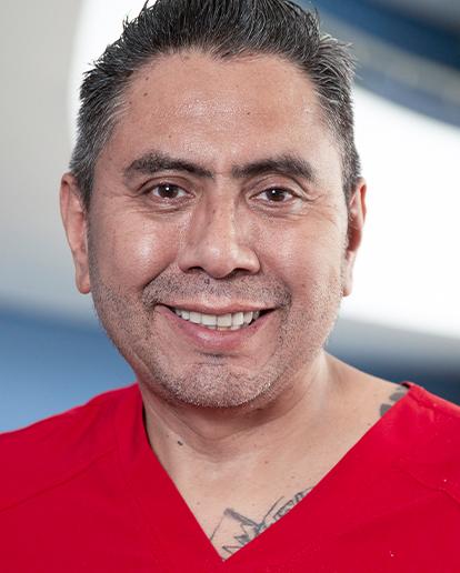 Es la foto de perfil de un ortopedista y traumatólogo en Huixquilucan de Hospital Angeles Lomas. Usa un uniforme rojo con cuello V. Tiene el cabello peinado hacia atrás.