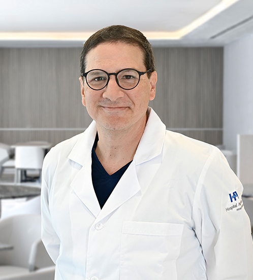 Es la foto de perfil de un ginecólogo en San Pedro Garza de Hospital Angeles Valle Oriente. Usa una bata blanca y lentes. Tiene el cabello café oscuro y los brazos cruzados por detrás.