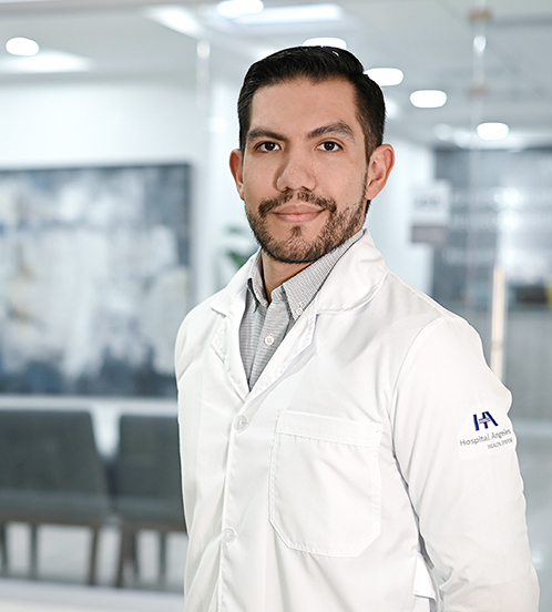 Es la foto de perfil de un ortopedista y traumatólogo en Ciudad de México de Hospital Angeles Acoxpa. Usa una bata blanca con una camisa de rayas grises con blanco. Tiene los brazos cruzados por detrás. Tiene barba y cabello café oscuro.