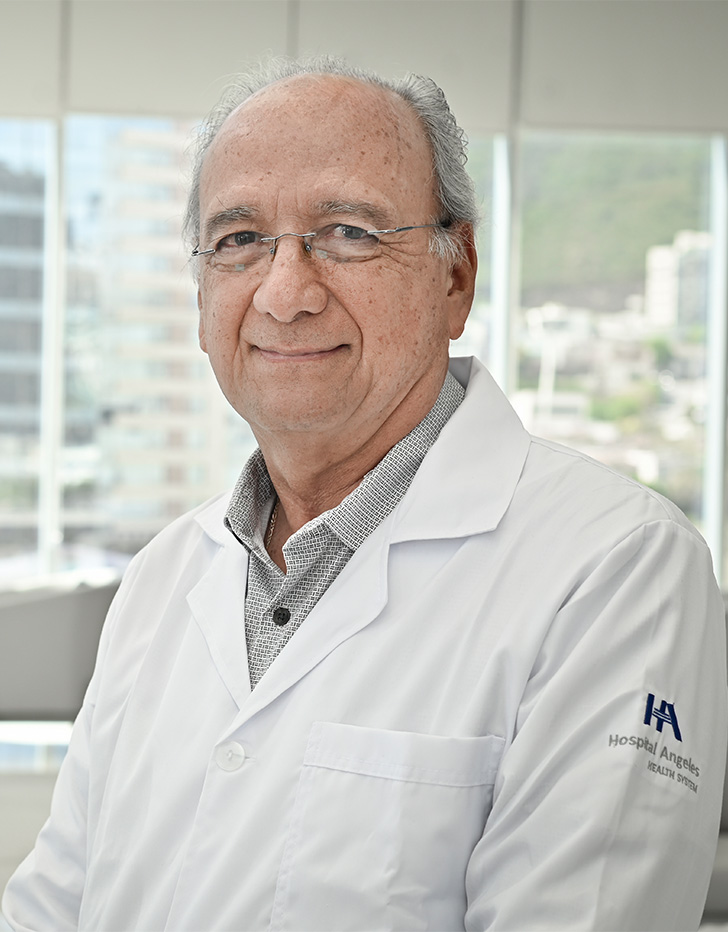 Es la foto de perfil de un cardiólogo intervencionista, cardiólogo e internista en San Pedro Garza de Hospital Angeles Valle Oriente. Usa una bata blanca con una camisa café claro. Tiene el cabello canoso y usa lentes.