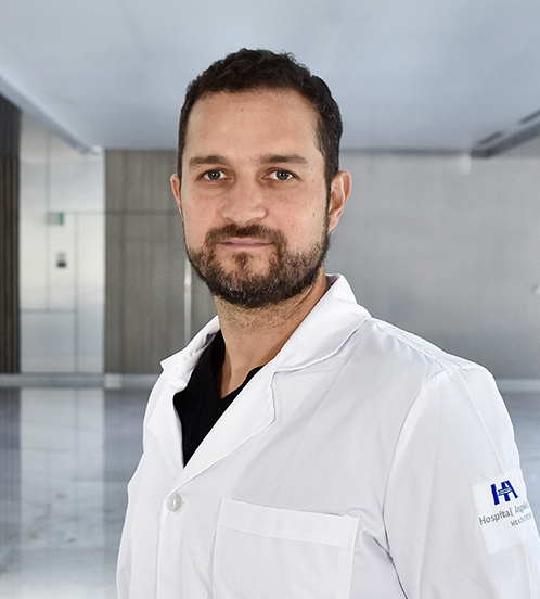 Es la foto de perfil de un otorrinolaringólogo en Querétaro de Hospital Angeles Centro-sur. Está parado de perfil. Usa una bata blanca, uniforme médico azul y tiene el cabello y barba color café oscuro.