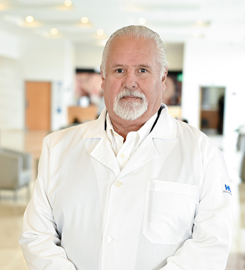 Es la foto de perfil de un ginecólogo en Xalapa de Hospital Angeles. Usa una bata blanca y un uniforme médico negro. Tiene el cabello y barba gris.