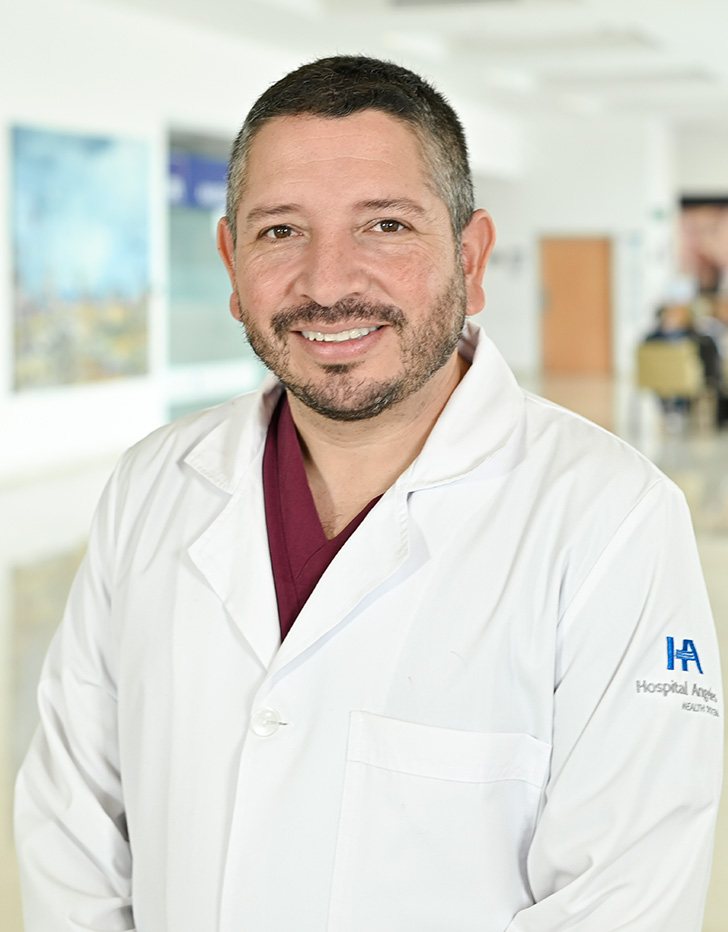 Es la foto de perfil de un ortopedista y traumatólogo en Xalapa de Hospital Angeles. Usa una bata blanxca con una camisa azul oscuro. Tiene el cabello negro. Está sonriendo ligeramente.