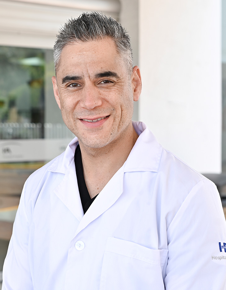 Es la foto de perfil de un anestesiólogo en Tijuana de Hospital Angeles. Usa un saco negro con una camisa blanca. Tiene el cabello gris con negro. Está sonriendo.