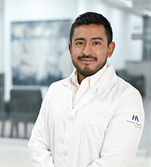 Es la foto de perfil de un cardiólogo en Ciudad de México de Hospital Angeles Acoxpa. Uso bata y camisa blanca. Tiene barba y cabello negro. Sus manos están al frente.