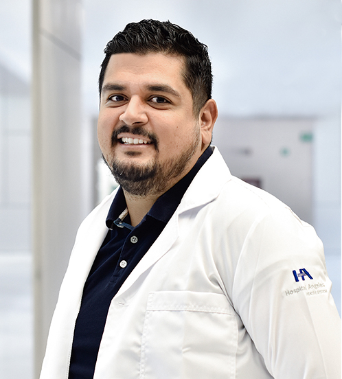Es la foto de perfil de un cirujano oncológico en Querétaro de Hospital Angeles Centro Sur. Usa una bata blanca con una camisa negra, barba de candado y está sonriendo.