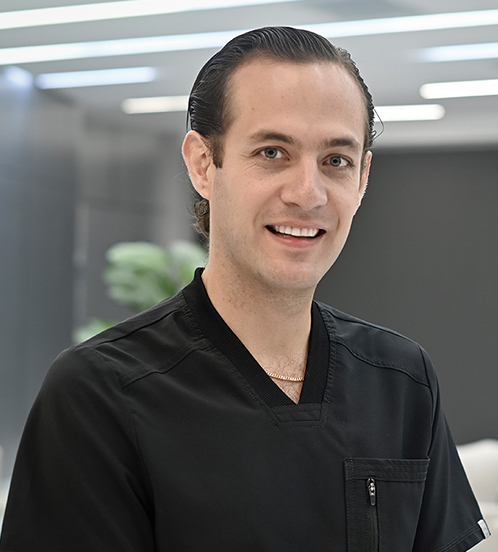 Es la foto de perfil de un ortopedista y traumatólogo en Querétaro de Hospital Angeles Centro Sur. Usa un uniforme de color negro en cuello V y está sonriendo.