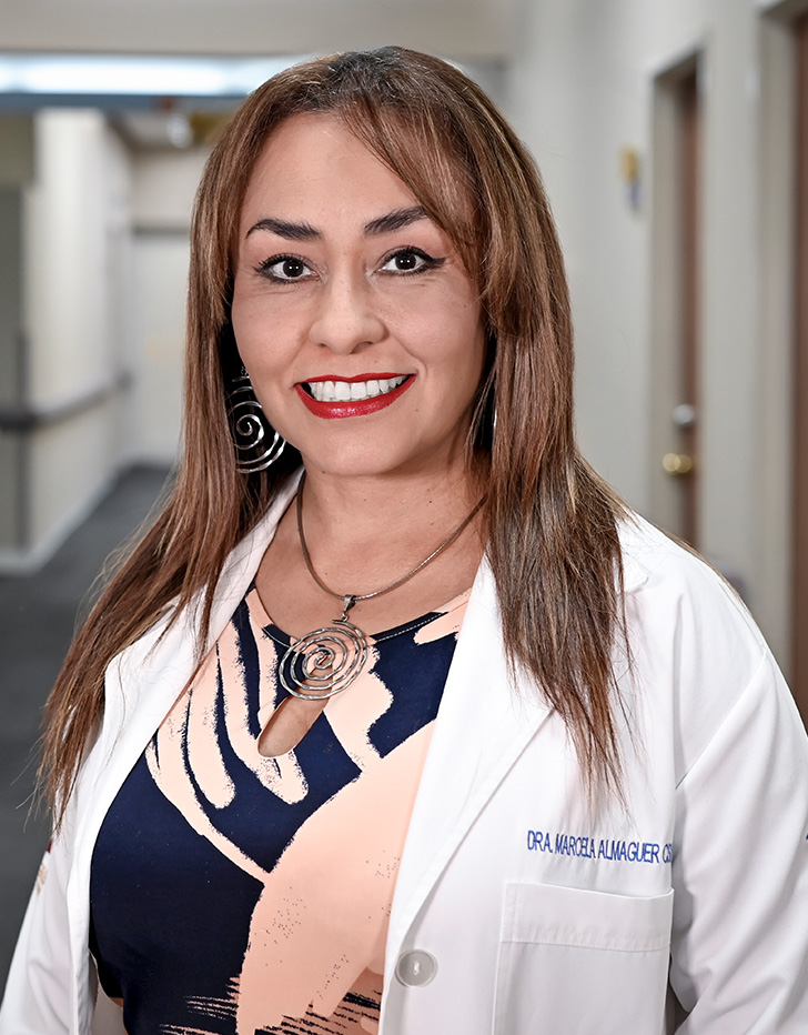 Es la foto de perfil de una ginecóloga y obstetra en Torreón de Hospital Angeles. Usa una bata blanca con una blusa amarilla. Tiene el cabello chino, corto y pelirojo. Está sonriendo.