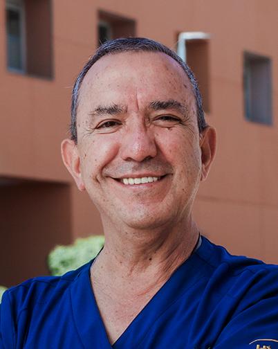 Es la foto de perfil de un otorrinolaringólogo en Torreón de Hospital Angeles. Usa un uniforme médico azul oscuro. Tiene el cabello negro con gris. Está sonriendo.