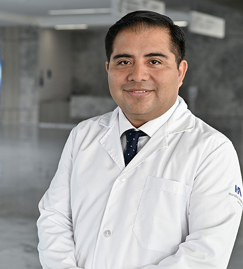 Es la foto de perfil de un oncólogo médico en Querétaro de Hospital Angeles Centro-sur. Usa una bata y camisa blanca con una corbata azul oscuro. Tiene el cabello negro y está sonriendo ligeramente.