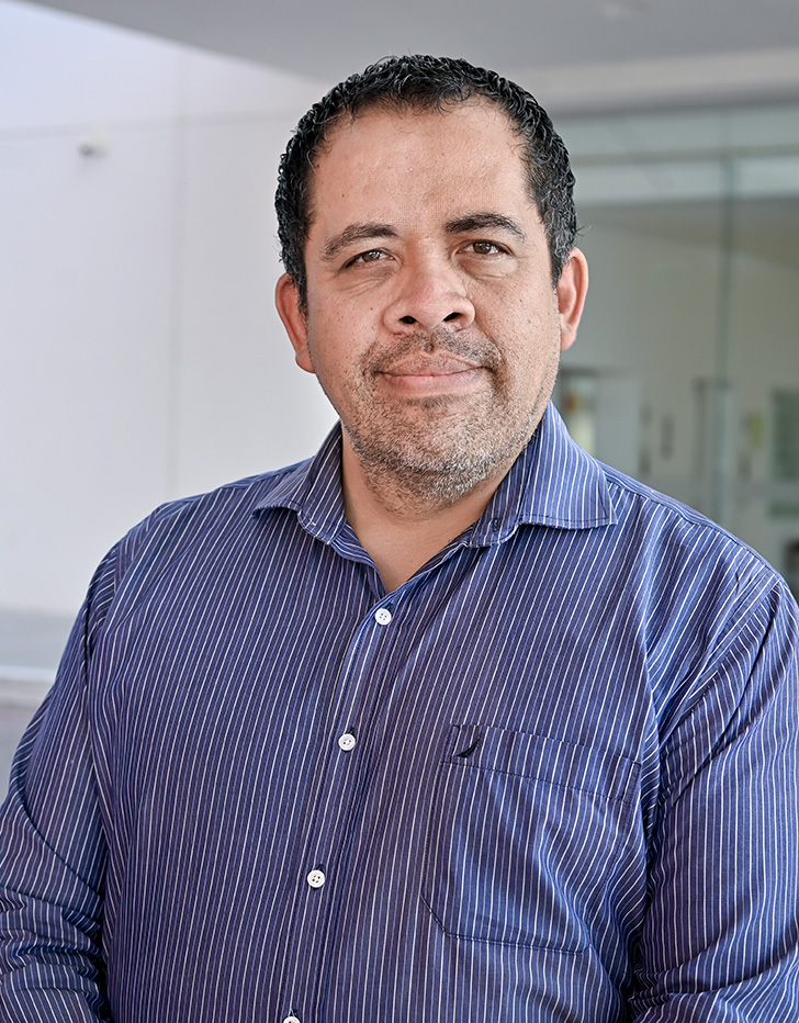 Es la foto de perfil de un especialista en radioterapia en León de Hospital Angeles León. Utiliza una bata blanca, tiene camisa azul y lineas blancas.