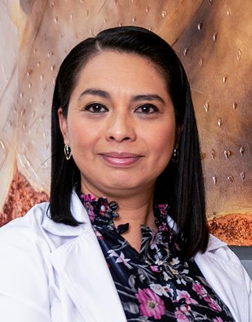 Es la foto de perfil de una hematóloga en León de Hospital Angeles León. Tiene una bata blanca, y una blusa negra con flores fiushas. Su cabello es negro y lacio.