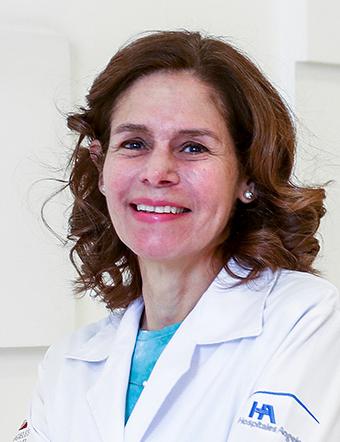 Es la foto de perfil de una dermatóloga en León de Hospital Angeles León. La doctora tiene una bata blanca con una blusa azul, su cabello es ondulado de color castaño claro.